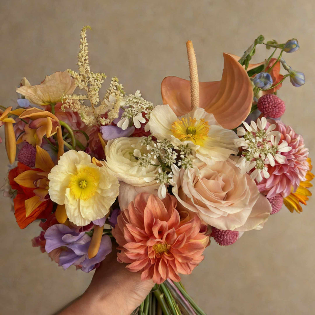 Bouquet of colorful flowers held by a hand against a neutral background