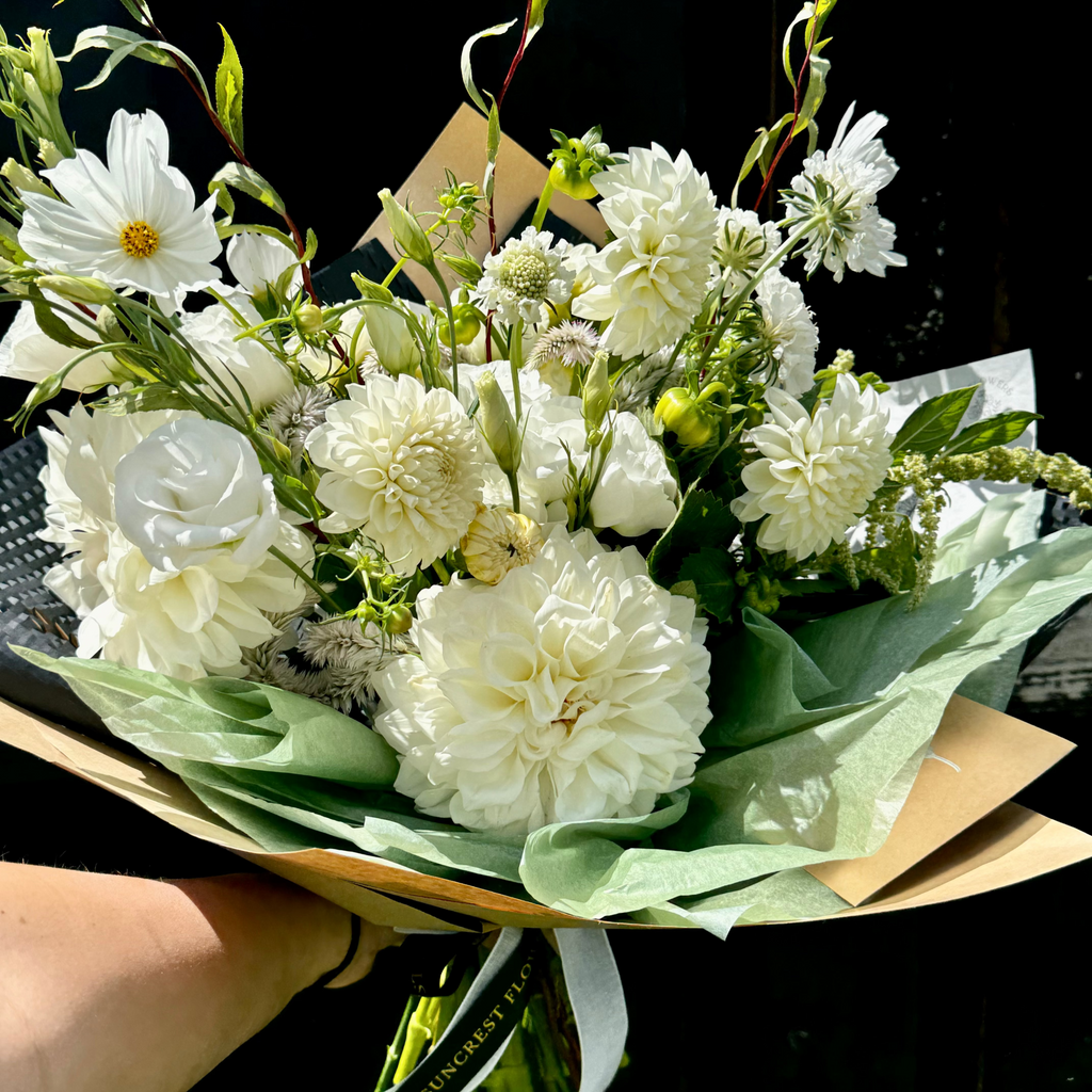 Bouquet of white flowers with green leaves held against a black background