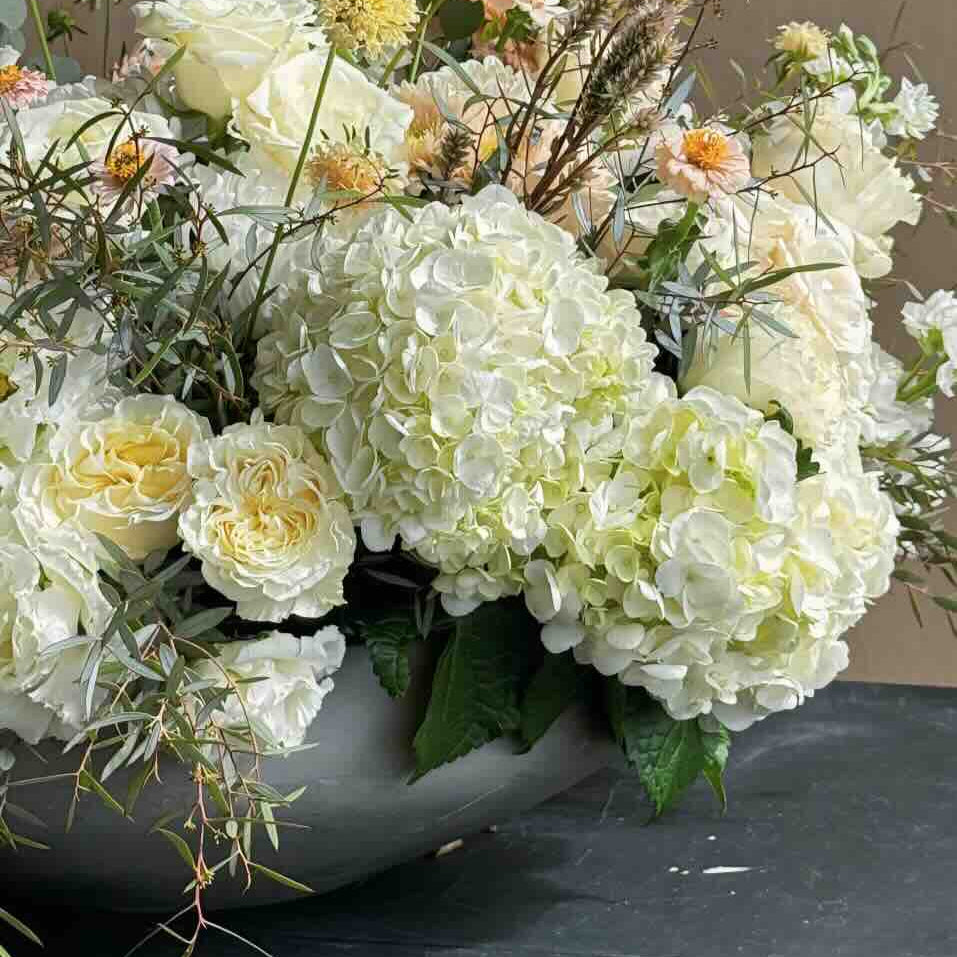 Floral arrangement with white hydrangeas and other flowers in a pot on a dark surface.