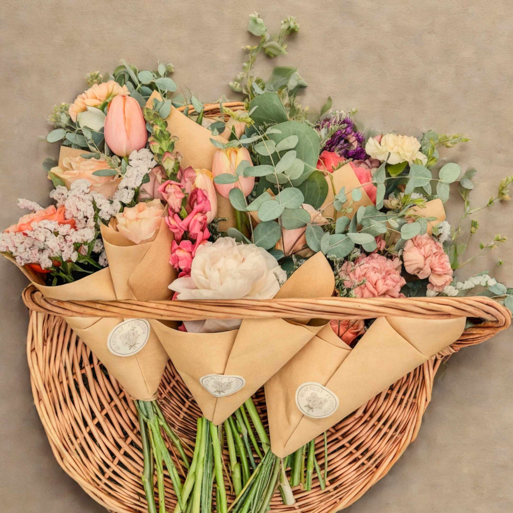Wicker basket filled with wrapped flowers and greenery on a neutral background